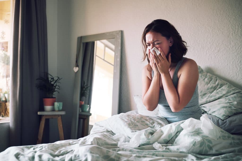 Woman in bed blowing her nose.