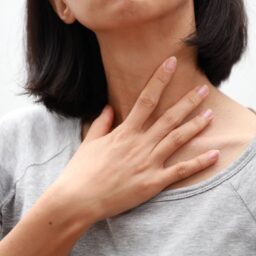 Woman with laryngitis putting her hand on her throat.