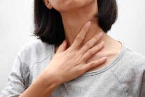 Woman with laryngitis putting her hand on her throat.