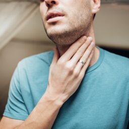 Close-up of a man touching his sore throat.