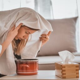 Woman with a towel over her head breathing in steam from a bowl