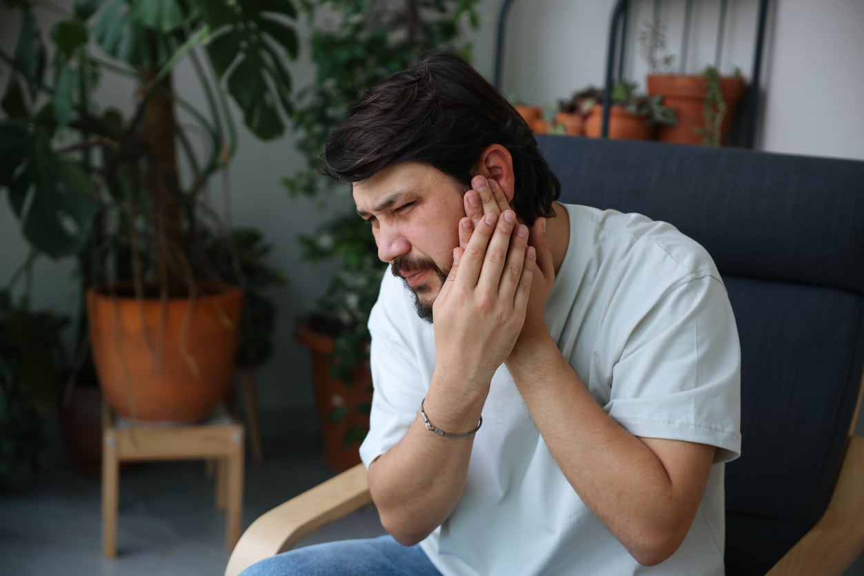 Man with ear pain holding his left ear.
