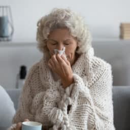 Senior woman wrapped up in a blanket blowing her nose