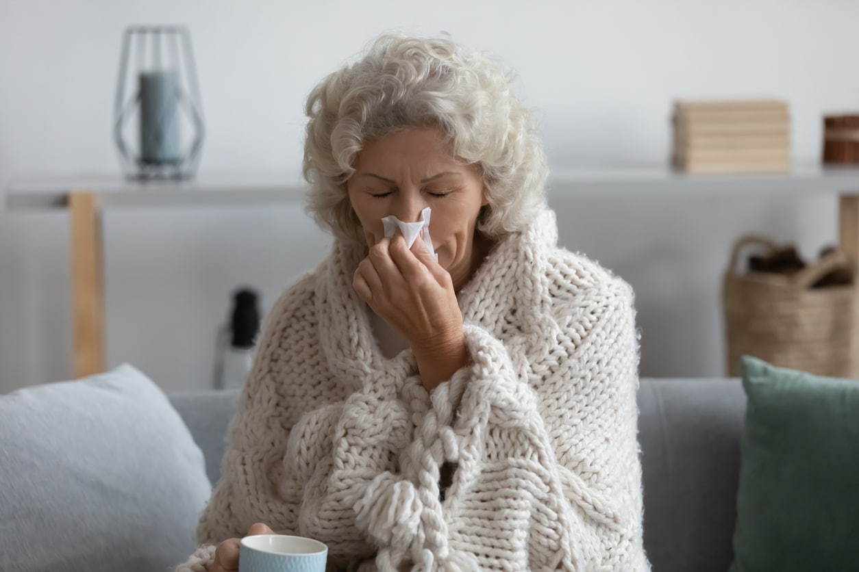 Senior woman wrapped up in a blanket blowing her nose.