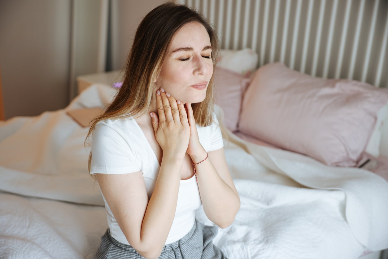 Woman holding her sore throat while sitting in bed.