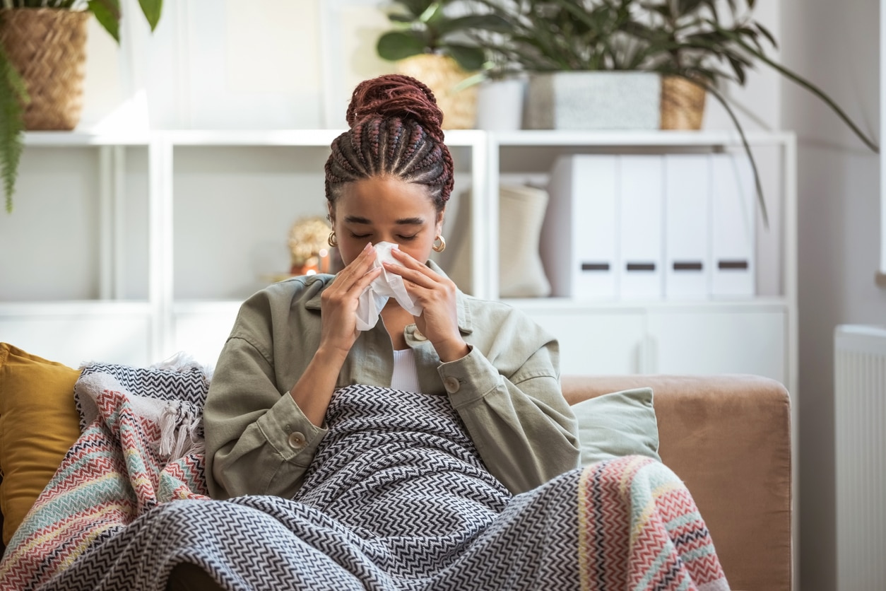 Woman sitting on the couch blowing her nose.